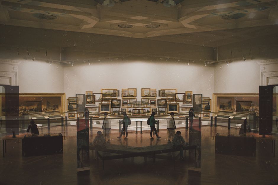 An elegant, high-ceilinged event hall with a curved, ornate white ceiling featuring multiple arched skylights that allow natural light to fill the space. The room has a polished wooden parquet floor and large windows along the far wall, framed by dark curtains. In the foreground, two long banquet tables are arranged parallel to each other, covered with pristine white tablecloths. The tables are set with neatly folded napkins, glassware, and tableware, indicating preparations for a formal gathering. Gold-colored Chiavari chairs with padded seats are evenly spaced along both sides of the tables, enhancing the sophisticated ambiance. The overall setting appears well-maintained and ready for an event, with no visible clutter or rubbish, consistent with professional venue management and private event arrangements, aligning with the context of alternative waste handling and event clearance services that Rubbish Removal Dulwich offers for such locations.